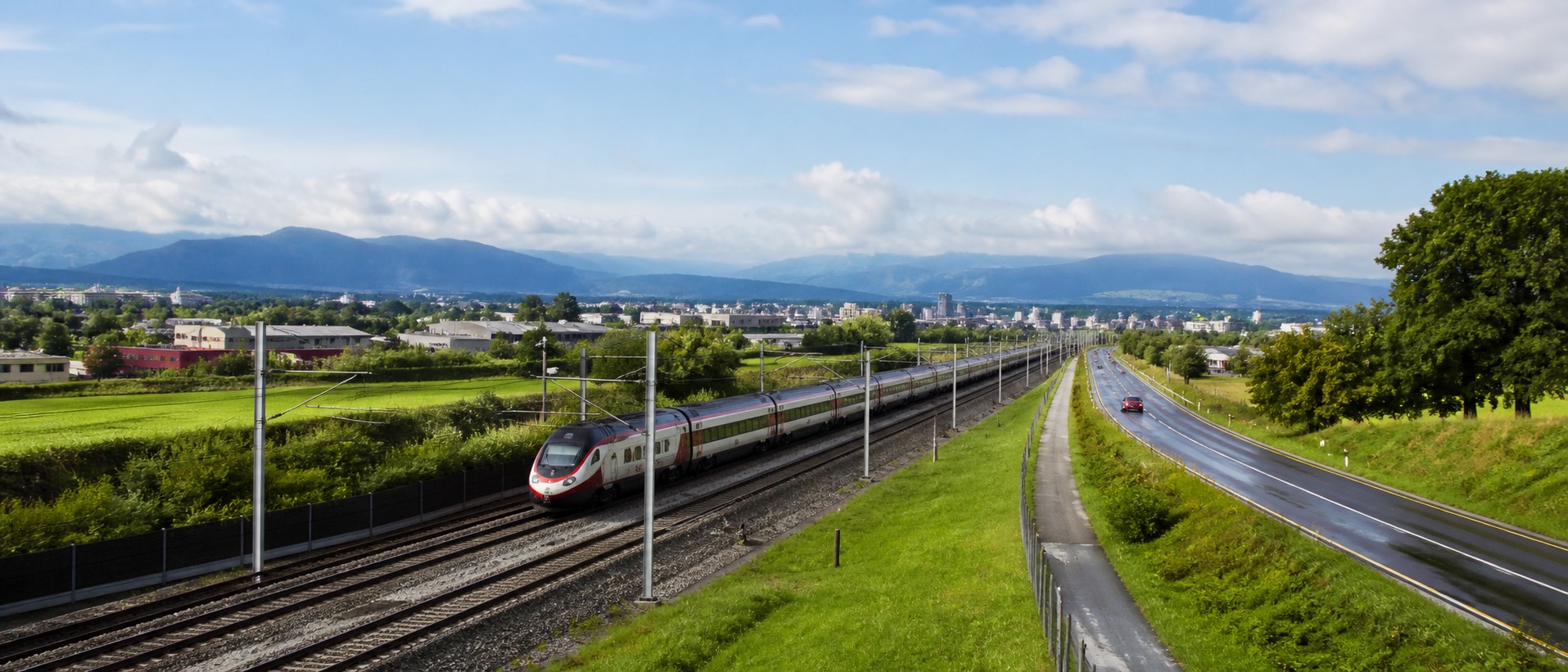 Rail and road routes move through a green European landscape under an open sky.